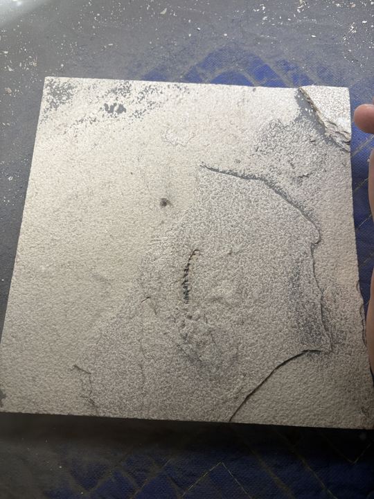A small square limestone slab held in one hand, with only a faint dark trace visible near the centre